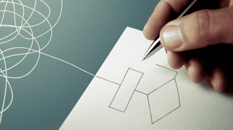 A person's hand holding a pen drawing connecting geometric shapes on paper, with an abstract pattern of white loops on a dark background.